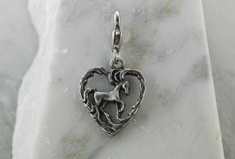 Silver heart-shaped horse themed jewelry pendant on a gray background.